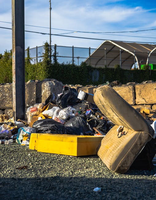 A large pile of mixed waste and rubbish, including various black and red garbage bags, crumpled cardboard boxes, flattened and partially opened parcels, and scattered paper and plastic packaging, situ